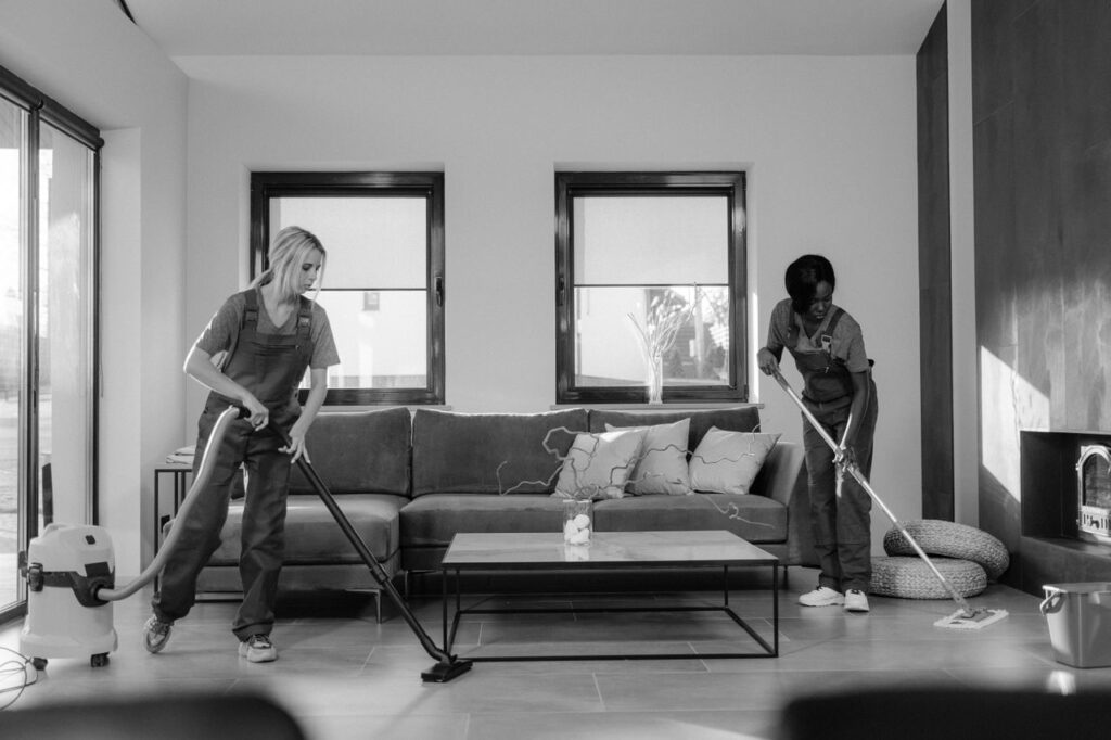 Crafting Captivating Headlines: Your awesome post title goes here Two women in work clothes cleaning a modern living room using a vacuum and mop.